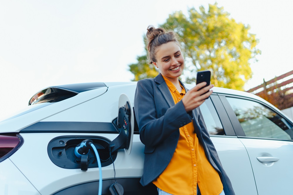 Frau-mit-Smartphone-beim-Laden-des-Elektroautos-umgeben-von-Elektrosmog